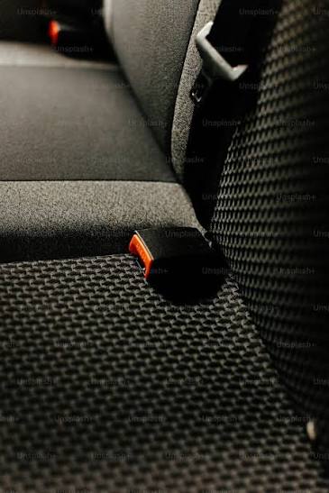Black seat belt buckle receiver on a short stalk emerging between the cushion and backrest of a rear car seat.