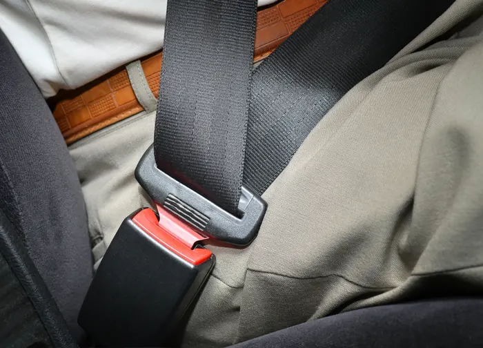 Fastened seat belt lying across an occupant's lap, showing the tongue engaged in the buckle receiver beside the seat.