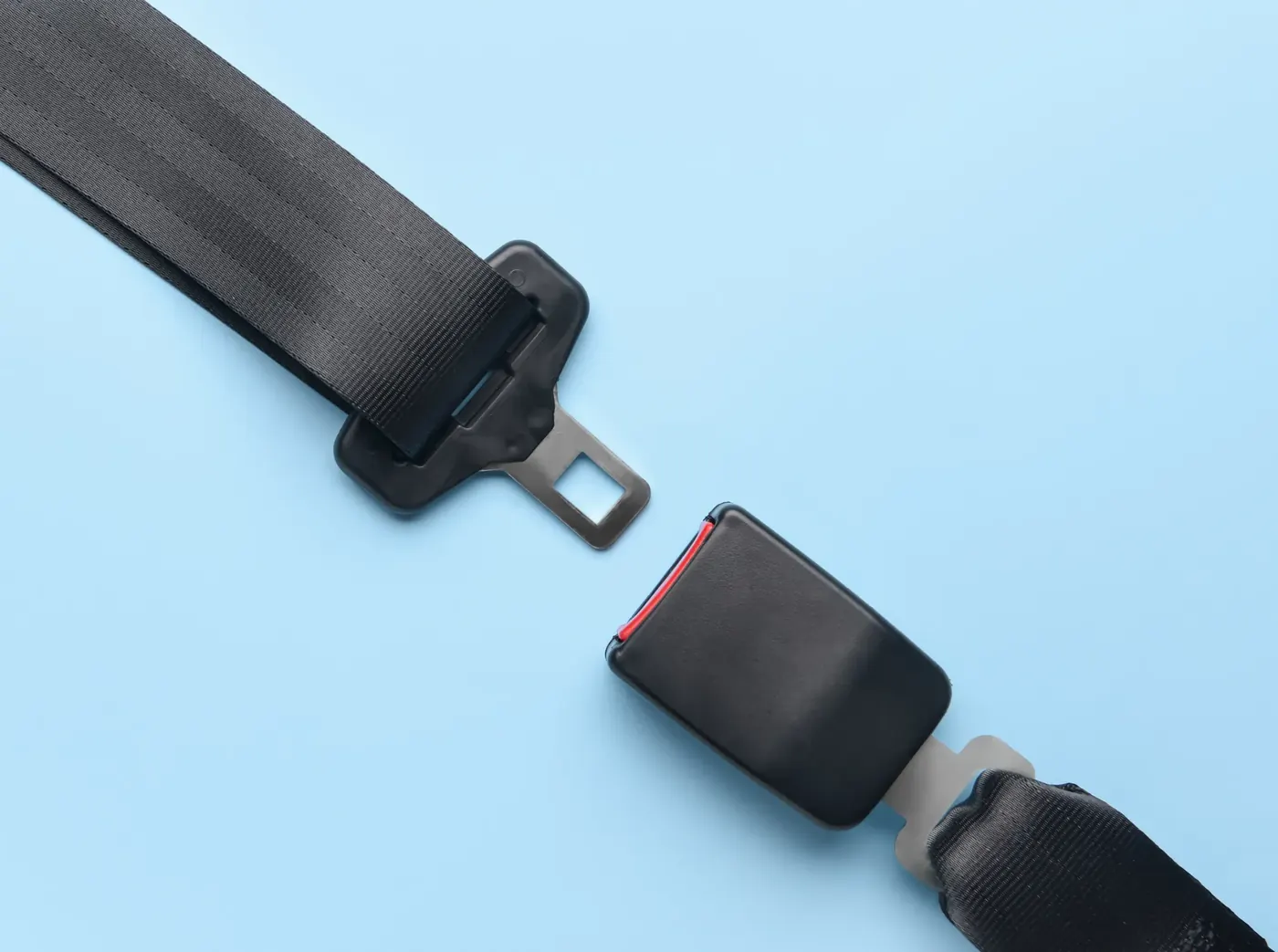 Replacement seat belt assembly photographed on a light blue background, showing black webbing, the metal tongue plate and the separate buckle receiver.