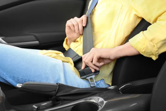 A person in a yellow shirt seated in a car, drawing the seat belt across and guiding the tongue plate toward the buckle receiver.